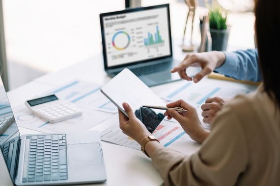 A busy desk with two laptops, one of which is displaying accounting software while someone reviews information on a tablet device