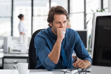 Man, blue shirt, glasses on the desk, looking at his computer screen with a despondent look on his face to depict how you might feel if can't pay your self assessment tax bill on time